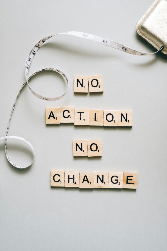 Scrabble tiles form motivational message ‘No Action No Change’ with a measuring tape.