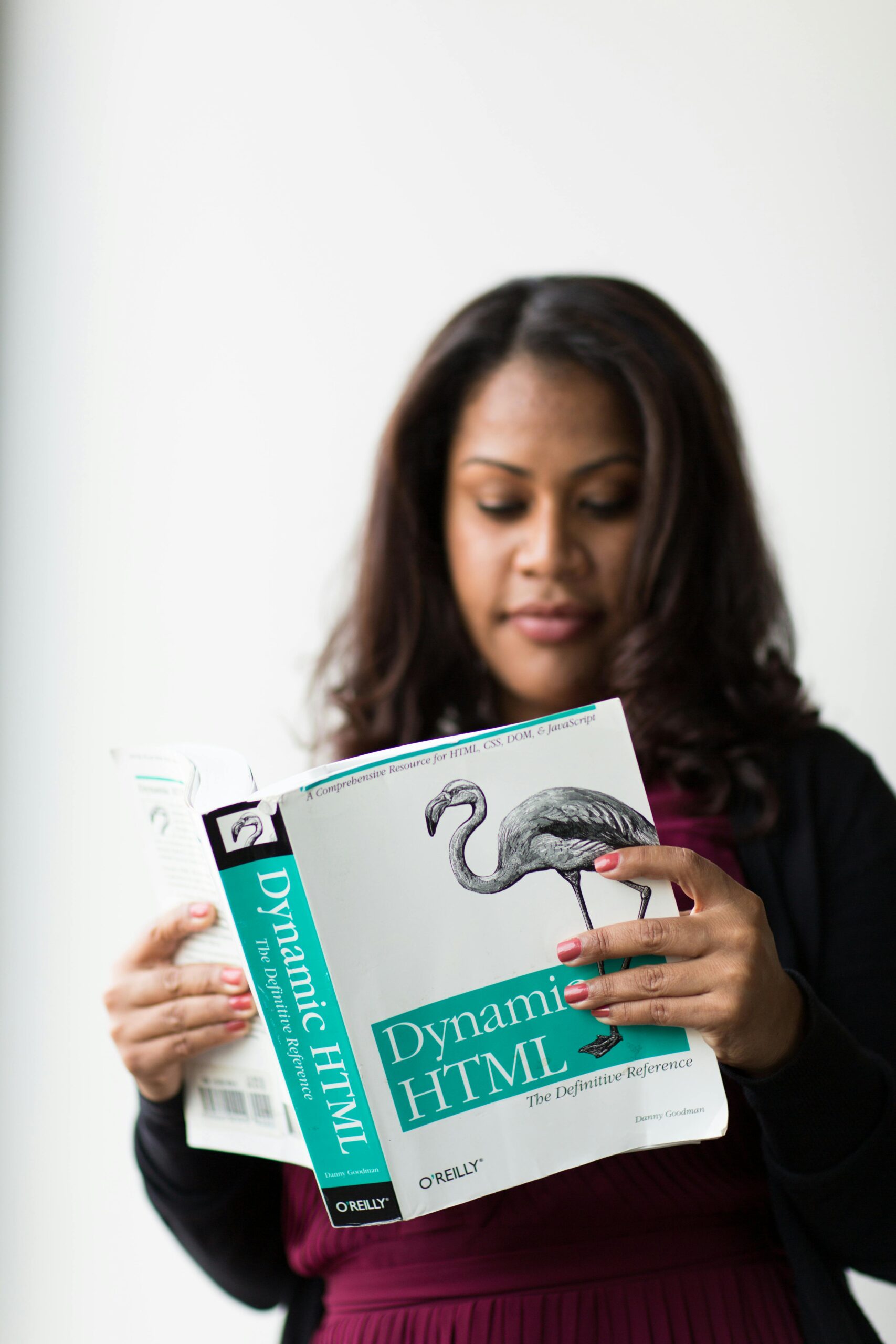 A woman focused on reading a book about Dynamic HTML indoors.